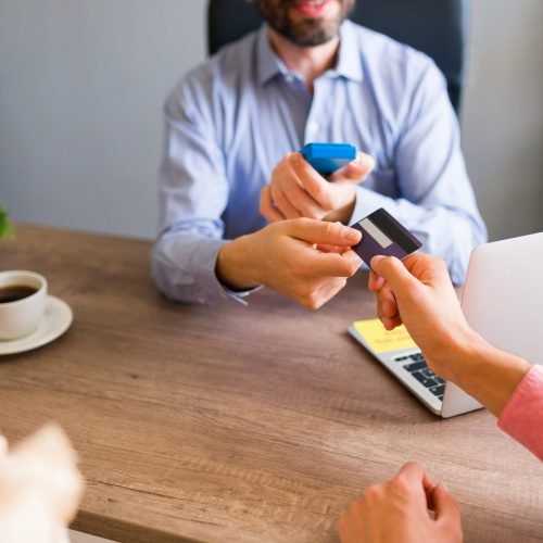 Close up of an hispanic man giving his credit card to a sales representative at the travel agency to pay for his business trip or holiday vacation